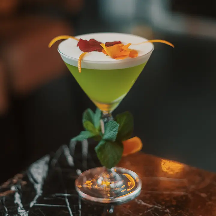 cicchetti-lounge-york-green-cocktail Green cocktail topped with foam, flower petals and citrus peel in a stemmed glass at Cicchetti Lounge in York.