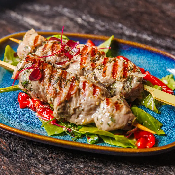 cicchetti-lounge-york-grilled-skewers Grilled meat skewers with mixed leaves, red peppers and microgreens on a blue plate at Cicchetti Lounge in York.
