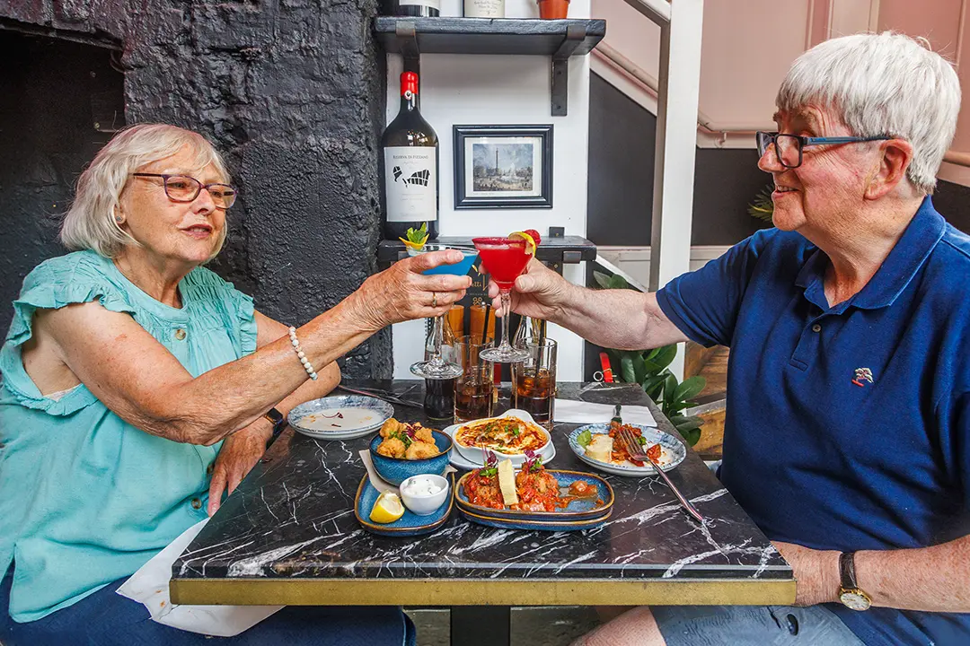 Two guests clink blue and red cocktails over Italian small plates at Cicchetti Lounge in York.
